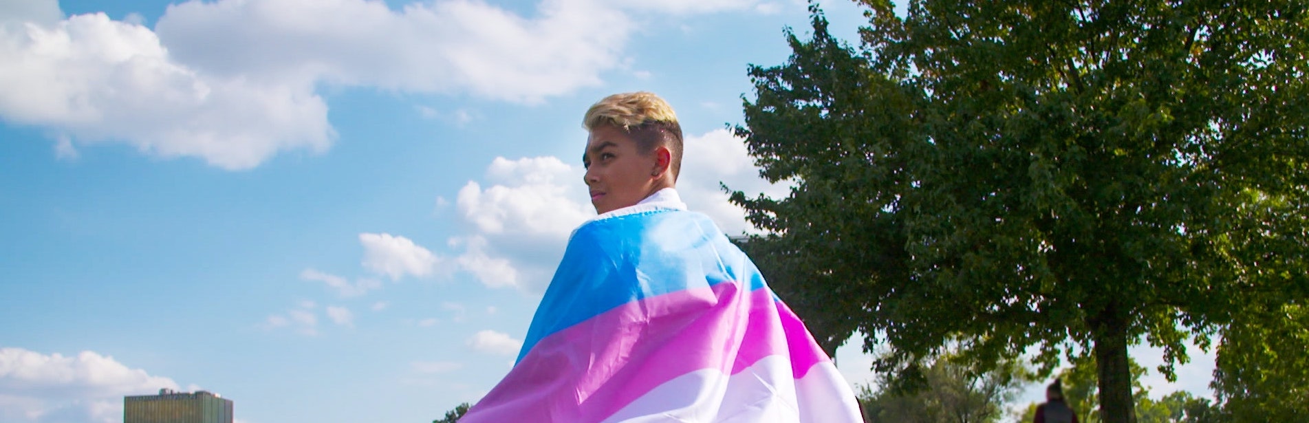 Young person draped in the trans pride flag — still from TRANSHOOD